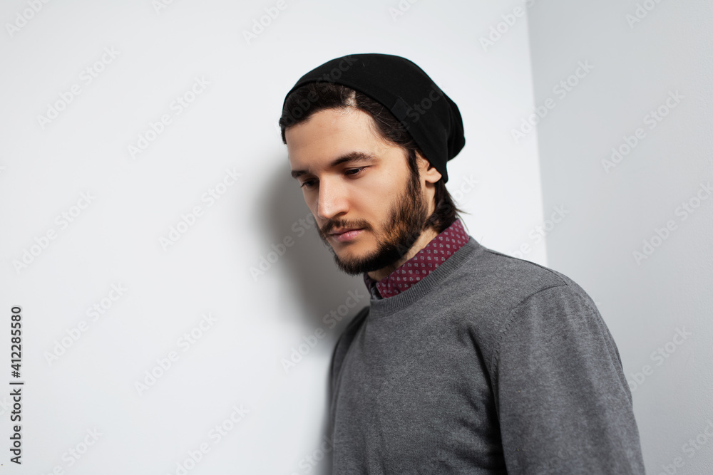 Studio side portrait of young guy on white background. Man wearing grey sweater and black hat. Studio side portrait of young guy on white background. Man wearing grey sweater and black hat.