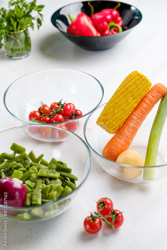 Raw vegetables lie in a glass bowl on the kitchen table. Prepare for cooking. Raw vegetables lie in a glass bowl on the kitchen table. Prepare for cooking.