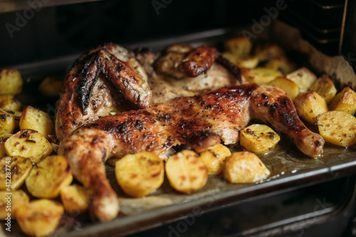 Grilled or roasted Chicken Tobacco on paper over baking sheet . Homemade freshly baked whole juicy chicken with potatoes, herbs, pepper. Selective focus, close up view. Organic country food.