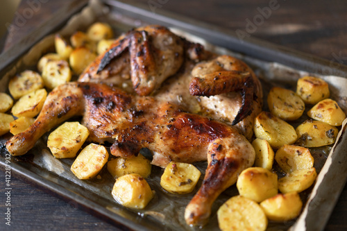 Grilled or roasted Chicken Tobacco on paper over baking sheet . Homemade freshly baked whole juicy chicken with potatoes, herbs, pepper. Selective focus, close up view. Organic country food.
