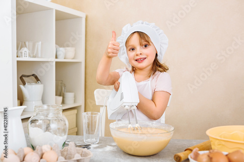 A cheerful young mother's assistant kneads the dough for a pie with a mixer, performs a step-by-step recipe on a tablet