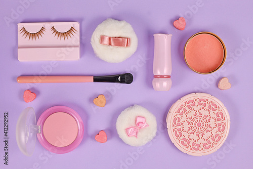 Cute pink makeup beauty products like brushes, fake lashes, powder or lipstick arranged on pastel violet background
