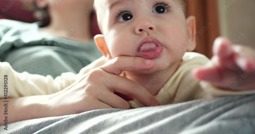 a young mother is holding a beautiful seven-month-old son who smiles and gnaws at fingers and mother's hand. itchy teeth of a newborn, teething a young mother is holding a beautiful seven-month-old son who smiles and gnaws at fingers and mother's hand. itchy teeth of a newborn, teething