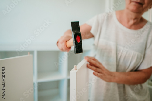 Middle-aged woman with white hair assembling new furniture for her home by herself. Close up..
