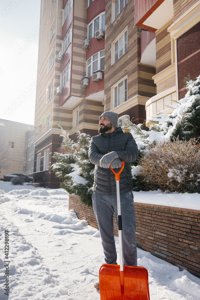 A young man clears the snow in front of the house on a sunny and frosty day. A young man clears the snow in front of the house on a sunny and frosty day.