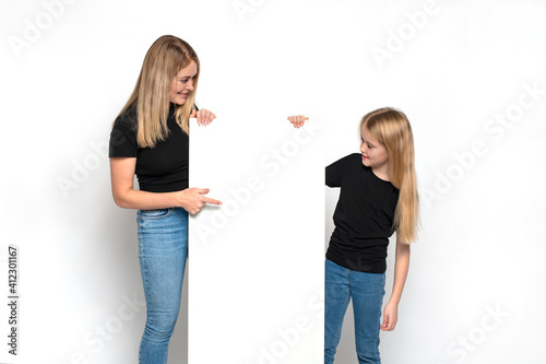 Young female shows index finger at blank poster to little girl, her daughter against white background photo