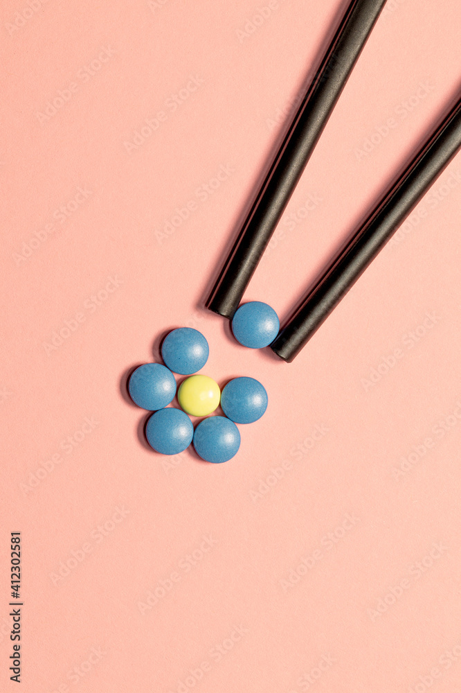 Flower made from pills and chopsticks isolated on pink background. Blue tablet or yellow painkiller as medical background. Pill for alleviating illness or fever. Vertical image Flower made from pills and chopsticks isolated on pink background. Blue tablet or yellow painkiller as medical background. Pill for alleviating illness or fever. Vertical image