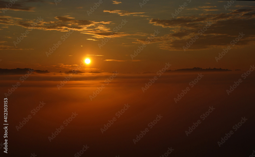 Sun rising above fog covered landscape in early summer morning