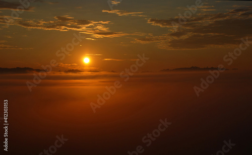 Sun rising above fog covered landscape in early summer morning