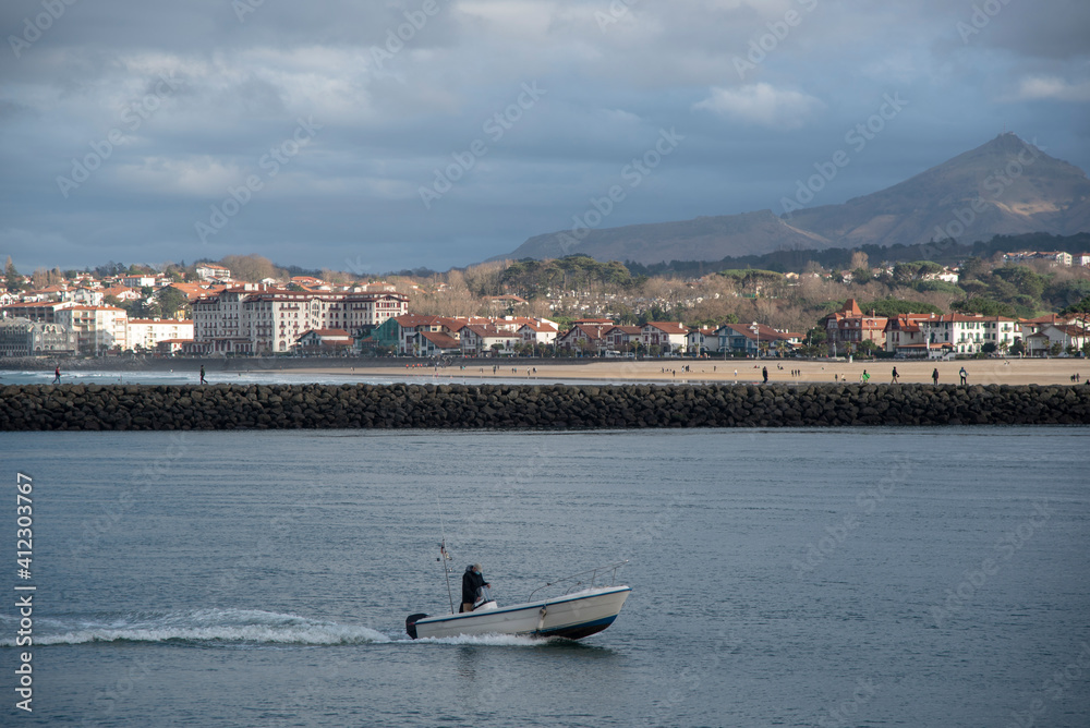 Obraz premium Un barco pequeño navegando por el rio en Hondarribia con Hendaya de fondo.