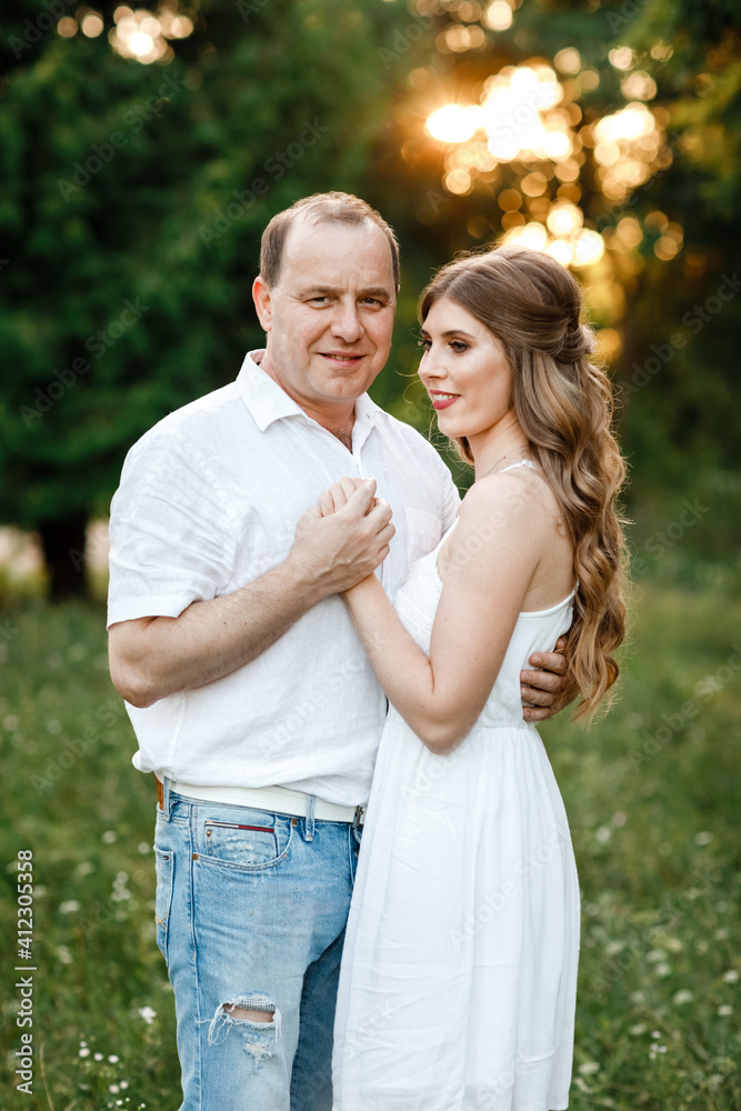 Fototapeta premium Young loving couple hugging on the green grass in the park. Beautiful woman and man gently touch each other. Beautiful couple in love. girl in the dress and the guy in the shirt. valentines day