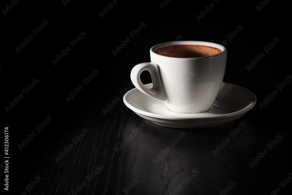 Cup of coffee on black wood table. White porcelain cup on saucer. Copy space.