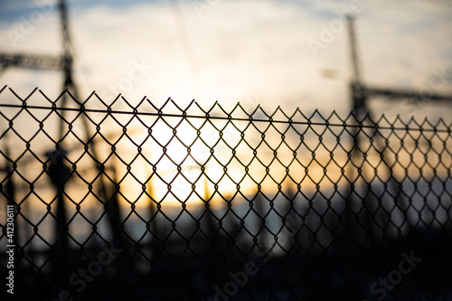 Fence sulfur of the power substation made of smooth wire braided into square meshes against the background of the setting sun.