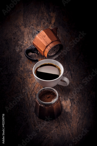 Fresh coffee mug and old rustic moka pot arrangement on dark brown wooden table studio shot
