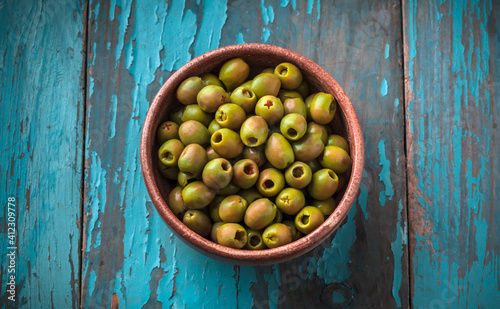 Green fresh olives served in crockery jar vibrant color arrangement on blue rustic wooden kitchen table studio shot
