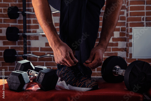 Fitness motivation and muscle training concept. Man in sneakers tying shoelaces in sunlight. Athlete starting exercise with dubbell weight. photo