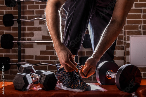 Fitness motivation and muscle training concept. Man in sneakers tying shoelaces in sunlight. Athlete starting exercise with dubbell weight. photo