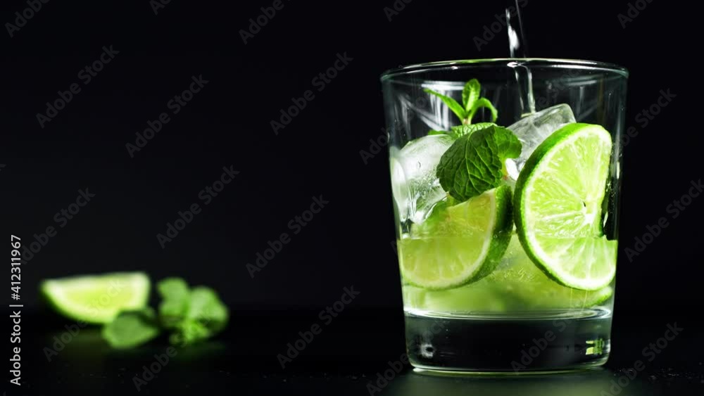 Close-up refreshing soda tonic. Pour carbonated water into a glass of lime and ice. Cold Mojito lemonade. Packshot. 4K UHD