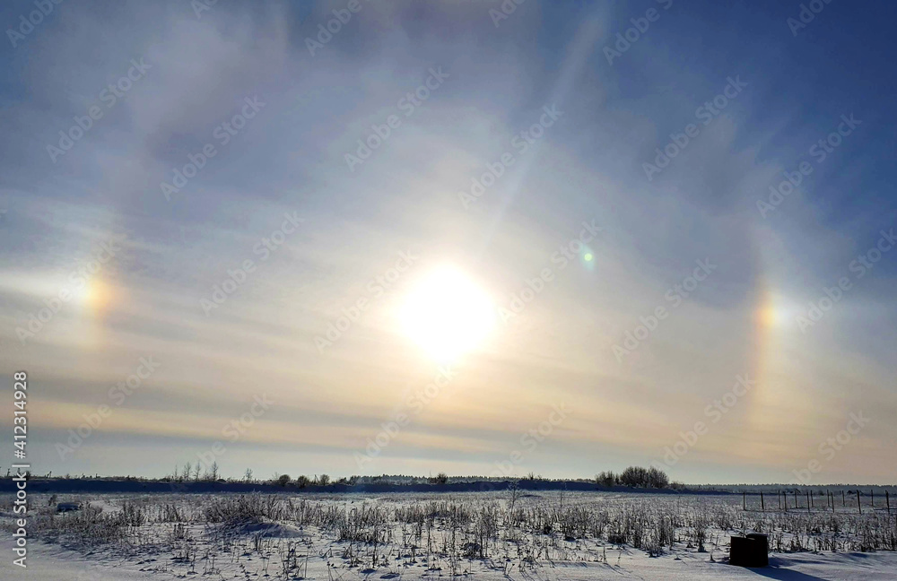 Halo around the sun on a winter, snowy day in a field against a blue sky