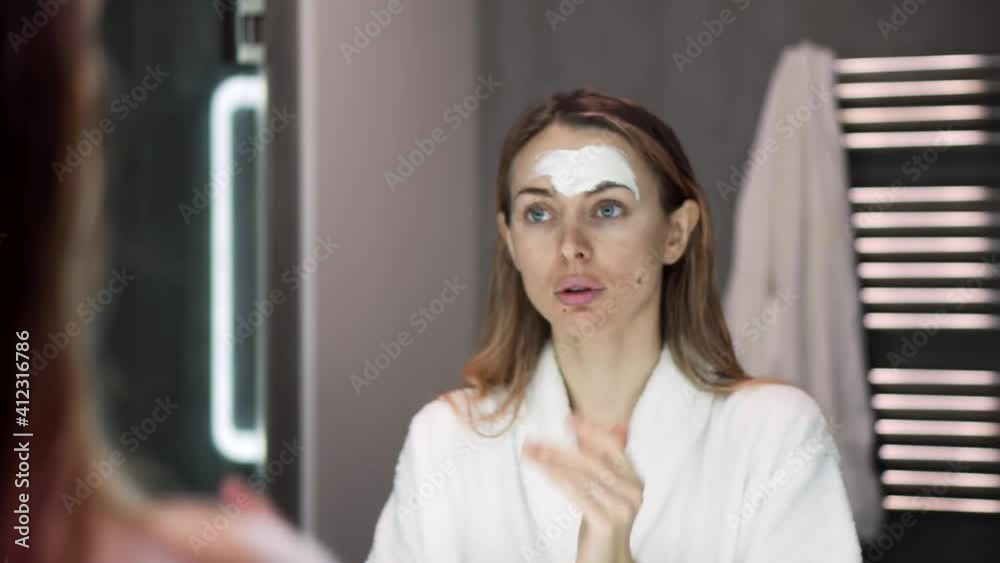 Portrait of a woman in bathrobe putting white mask for moisturizing using fingers Portrait of a woman in bathrobe putting white mask for moisturizing using fingers