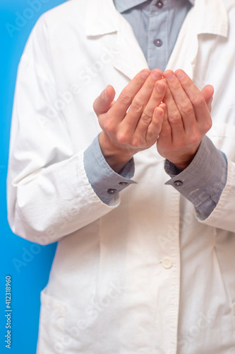 A young man in a white coat raised his hands up and pray. Blue background. Doctor praying. A Muslim makes dua