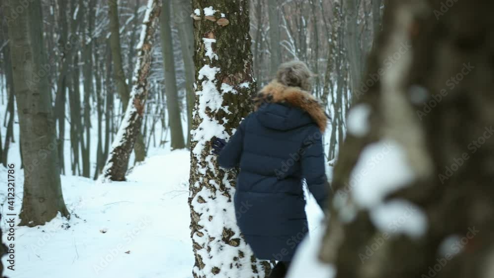 Portrait of a cute man peeking from behind tree. Woman hiding. Smiling attractive girl peeking out from behind trunk. Blind man's buff game, couple run after each other on snowy winter day Portrait of a cute man peeking from behind tree. Woman hiding. Smiling attractive girl peeking out from behind trunk. Blind man's buff game, couple run after each other on snowy winter day
