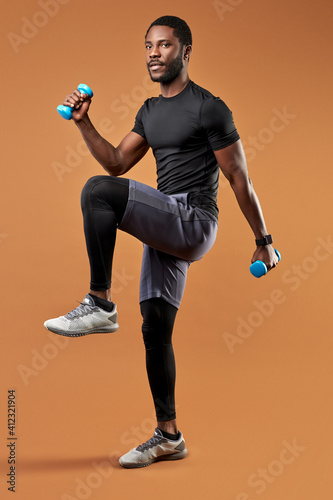 black athletic man do exercises with weights holding dumbbells in hands, isolated on brown background