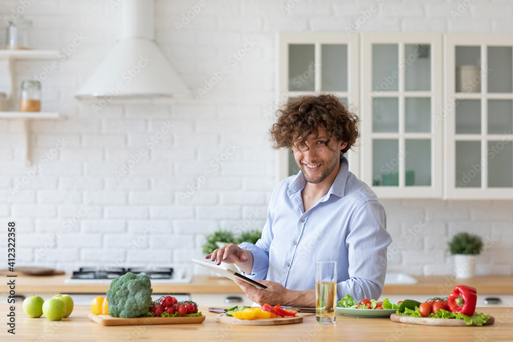 Young man watching video recipe on digital tablet while cooking vegetables in kitchen. Young man watching video recipe on digital tablet while cooking vegetables in kitchen.
