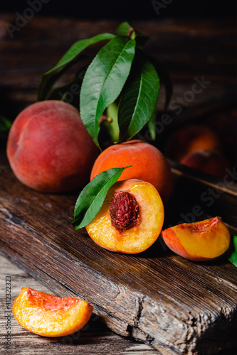 Juicy ripe peach on dark wooden rustic cutting board. Delicious farm peaches with leaves whole fruit in halves, peach with bone. Still life peach with in dark key. Vertical format