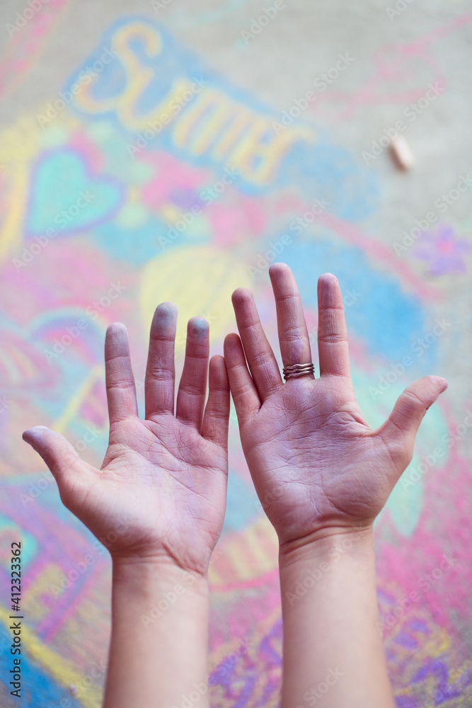 A young chalk artists dusty hands above a colourful pavement chalk drawing