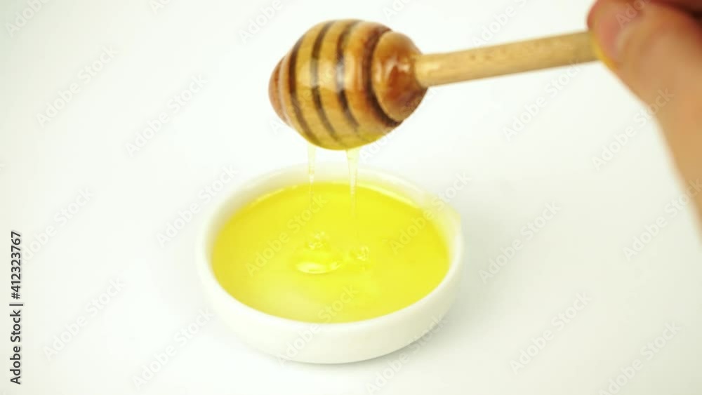 Liquid honey taking with wooden stick from small white plate Liquid honey taking with wooden stick from small white plate
