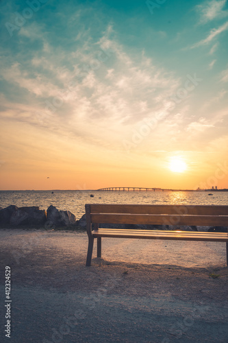 Isolated public bench at sunrise. Re island bridge in the background. portrait format