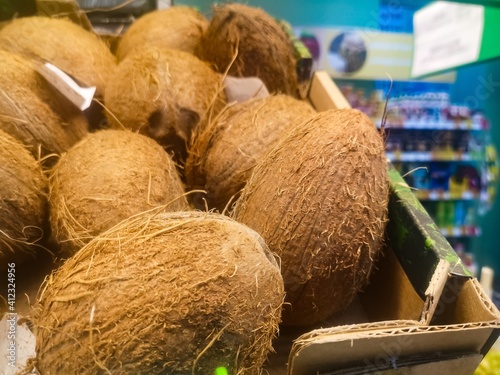 large ripe coconuts are sold in the grocery store on a shelf among vegetables and fruits
