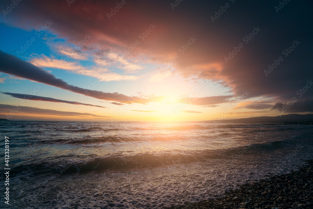 Dramatic colorful sunset on sea coast above water surface. Ocean waves splashes at beach coastline. Beautiful seascape and freedom concept.