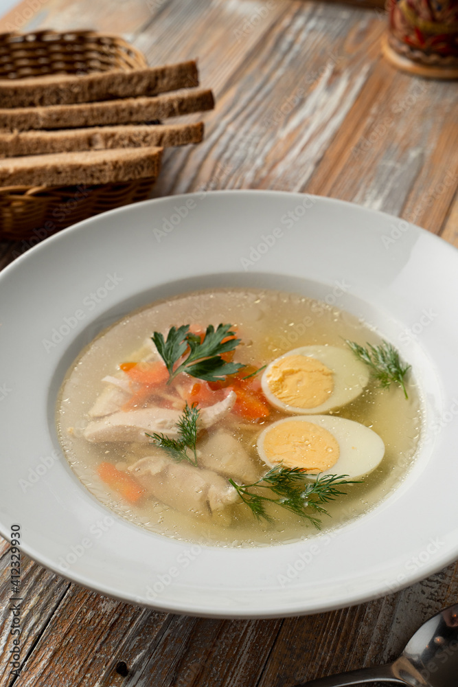 Simple chicken broth with egg and white meat, traditional treatment from cold and flu, served on rustic wooden table Simple chicken broth with egg and white meat, traditional treatment from cold and flu, served on rustic wooden table
