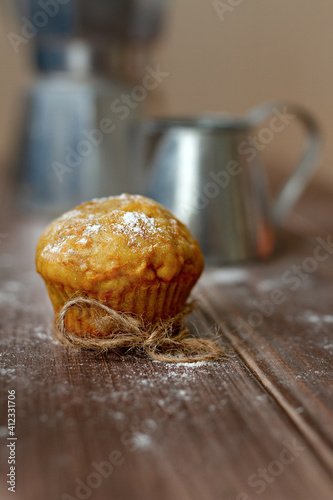 orange carrot cupcake with powdered sugar on wooden table against background of metal milk jug and coffee maker in blur, selective focus © ksenija1803z