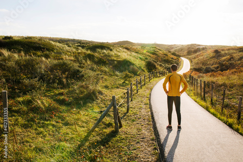 Young caucasian runner standing in the dunes during sunset.
