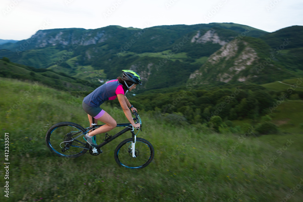Caucasian young female riding mountain bike downhill a green mea Caucasian young female riding mountain bike downhill a green mea