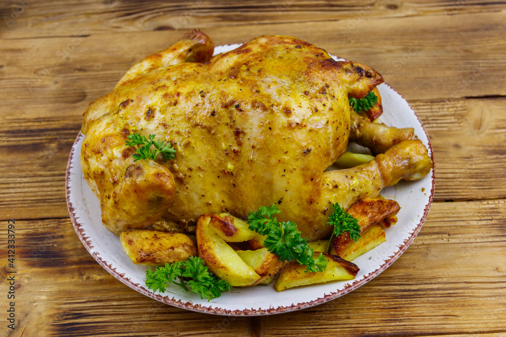 Baked whole chicken with potato on a wooden table