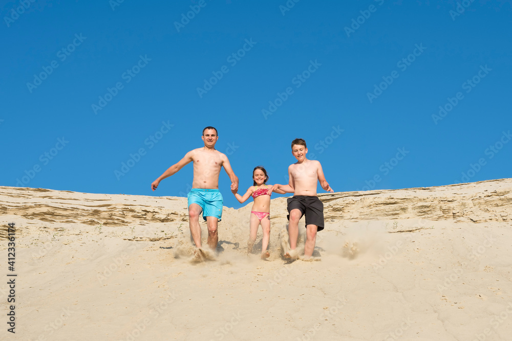 Father and children run to the beach sand on a sunny day. Seed on vacation. Recreation, sports, lifestyle