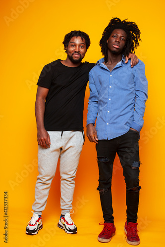 two african american guys posing cheerful together on yellow background, lifestyle people concept