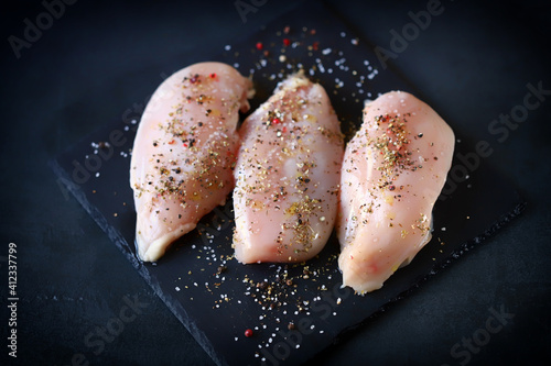 Selective focus. Raw chicken fillets with spices on a stone board. photo