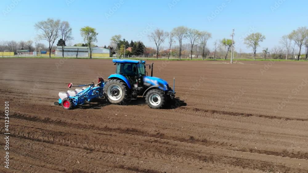 Aerial view of a farmer in tractor seeding corn. Drone sliding shot of planting agricultural crops at field near the road and tree line, cars passing by Aerial view of a farmer in tractor seeding corn. Drone sliding shot of planting agricultural crops at field near the road and tree line, cars passing by