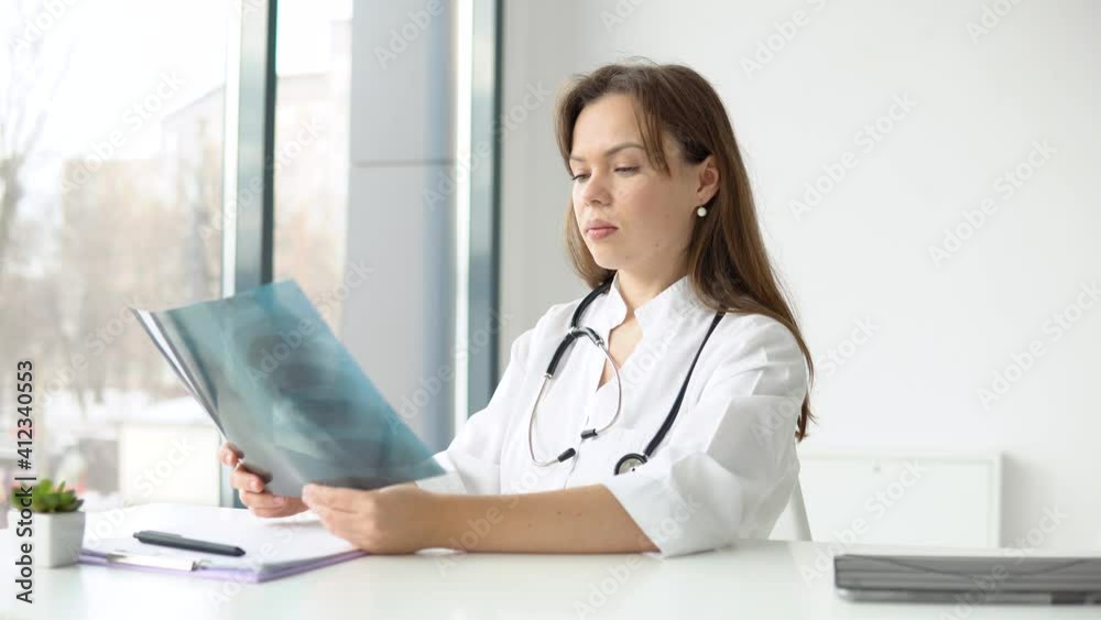 Young caucasian woman doctor wearing white medical coat and stethoscope holds the x-ray Young caucasian woman doctor wearing white medical coat and stethoscope holds the x-ray