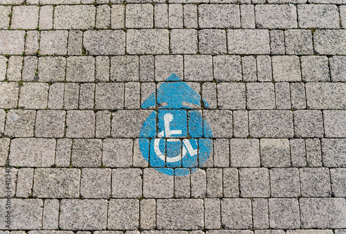 Handicapped wheelchair sign on a sidewalk, blue color on grey bricks, round-shaped, with arrow.  photo