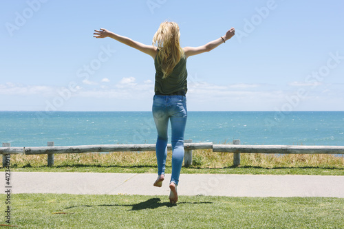 Teenage girl jumping for joy as she runs toward a view of the ocean.