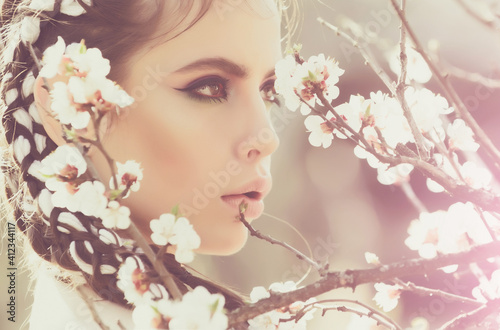 Spring girl and flowers. Pretty woman with flower blooming, fashionable makeup on face, outdoor, natural background. © Volodymyr