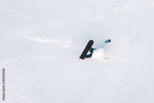 Male snowboarder falling down in powdery snow