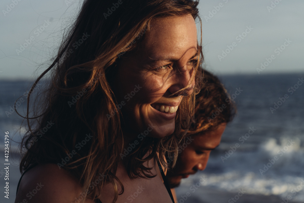 Against the ocean, two faces of a couple in love. in the foreground is a profile of a laughing girl while on a rear plan looking down a man. High quality photo
