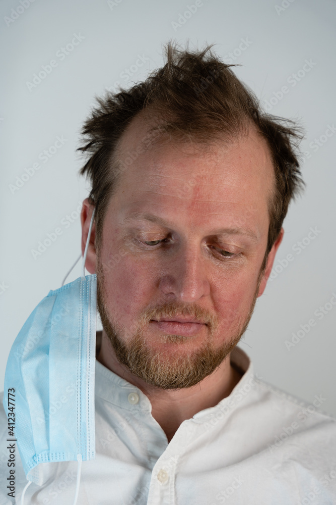 Close up portrait of a man with a smile on his face and a covid 19 protective mask on one side of his head looking straight down Close up portrait of a man with a smile on his face and a covid 19 protective mask on one side of his head looking straight down